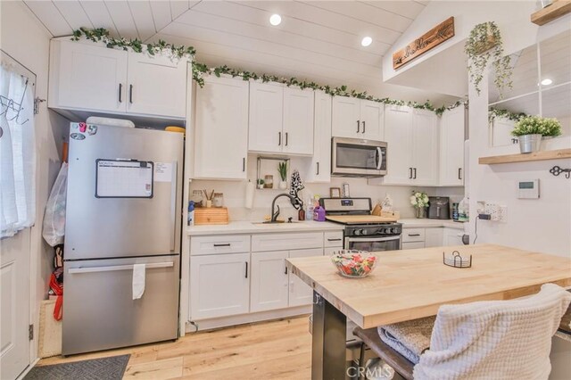 kitchen with vaulted ceiling, appliances with stainless steel finishes, butcher block countertops, sink, and white cabinets