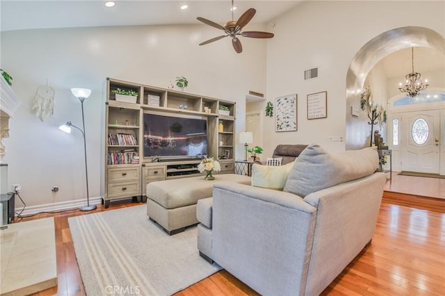 living room with high vaulted ceiling, ceiling fan with notable chandelier, and light hardwood / wood-style floors