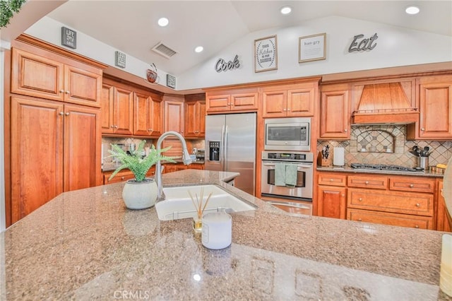 kitchen with lofted ceiling, sink, appliances with stainless steel finishes, custom range hood, and light stone countertops