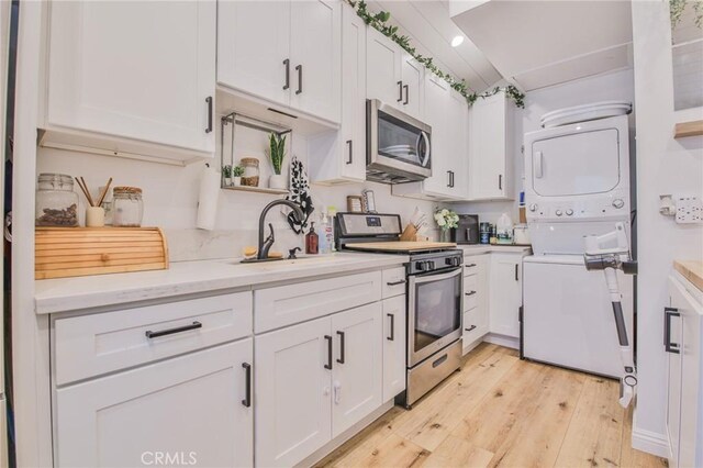 kitchen featuring white cabinetry, sink, stacked washer / drying machine, light hardwood / wood-style floors, and stainless steel appliances