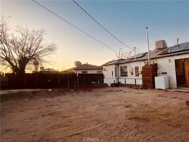 back house at dusk with central AC unit, washer / dryer, and solar panels