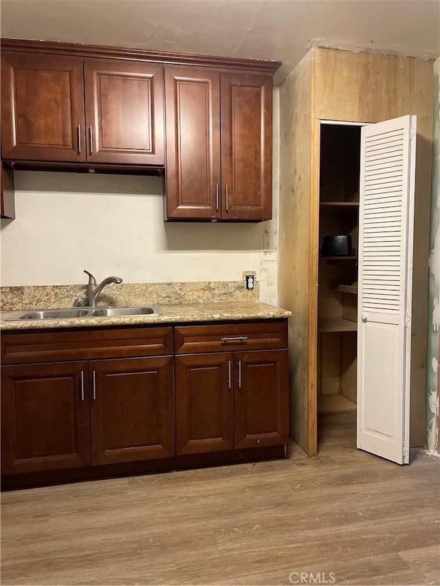 kitchen featuring light stone counters, dark brown cabinets, sink, and light hardwood / wood-style flooring