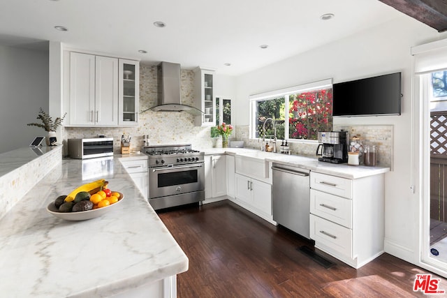 kitchen with wall chimney range hood, appliances with stainless steel finishes, white cabinetry, dark hardwood / wood-style floors, and light stone countertops