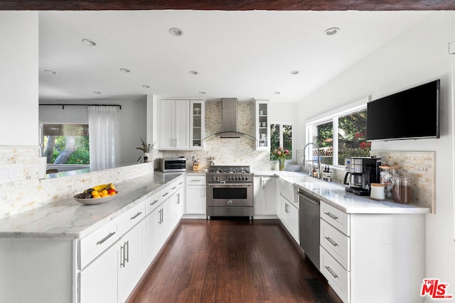 kitchen featuring stainless steel appliances, white cabinetry, kitchen peninsula, and wall chimney exhaust hood