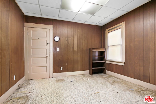 empty room with a paneled ceiling and wood walls