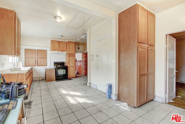 kitchen with tasteful backsplash, black range, tile countertops, and light tile patterned floors