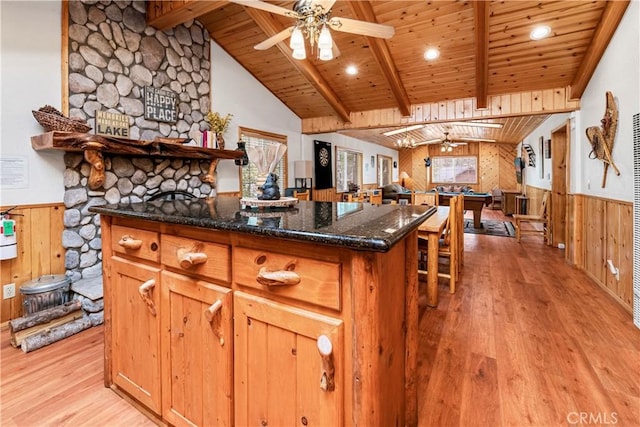 kitchen featuring wood walls, vaulted ceiling with beams, ceiling fan, wooden ceiling, and light hardwood / wood-style flooring