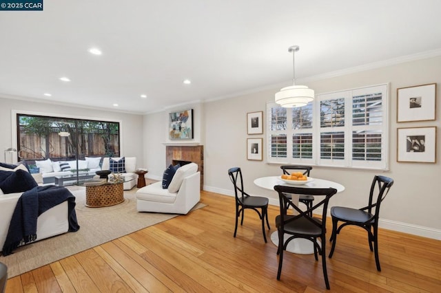 dining space featuring crown molding, a fireplace, and light hardwood / wood-style floors