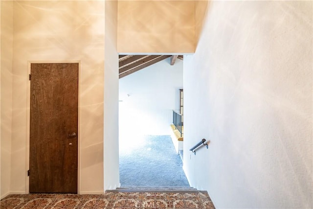 stairs with carpet floors and vaulted ceiling with beams