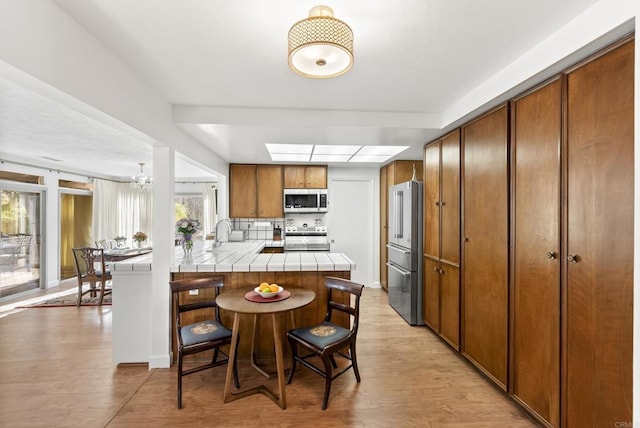 kitchen featuring a healthy amount of sunlight, stainless steel appliances, tile counters, and light wood-type flooring