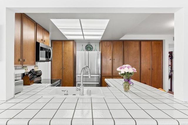 kitchen with appliances with stainless steel finishes, tile counters, and sink