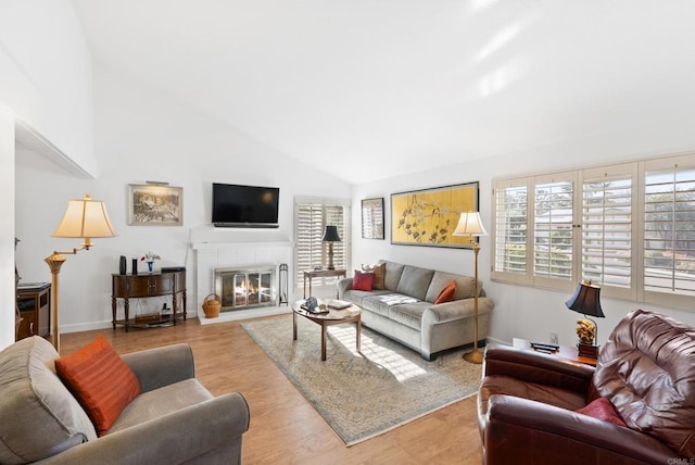 living room featuring a tiled fireplace, high vaulted ceiling, and light hardwood / wood-style floors