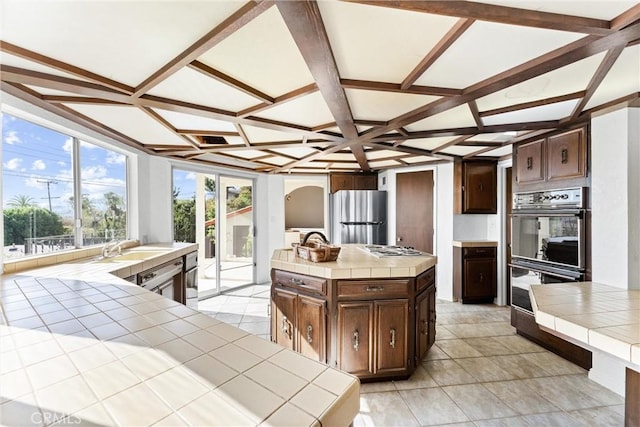 kitchen with coffered ceiling, appliances with stainless steel finishes, tile countertops, and a kitchen island