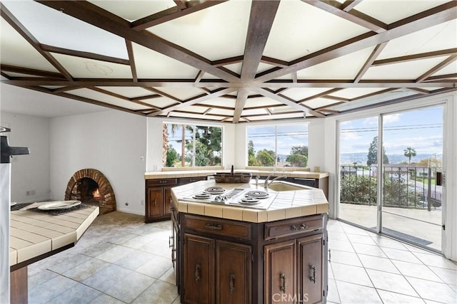 kitchen with tile countertops, white cooktop, sink, a center island, and dark brown cabinetry