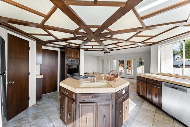 kitchen with appliances with stainless steel finishes, a kitchen island with sink, dark brown cabinetry, tile counters, and french doors