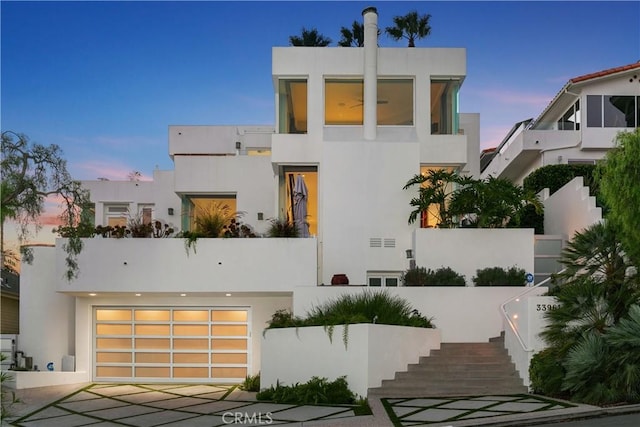 contemporary house with stucco siding, a garage, and stairway