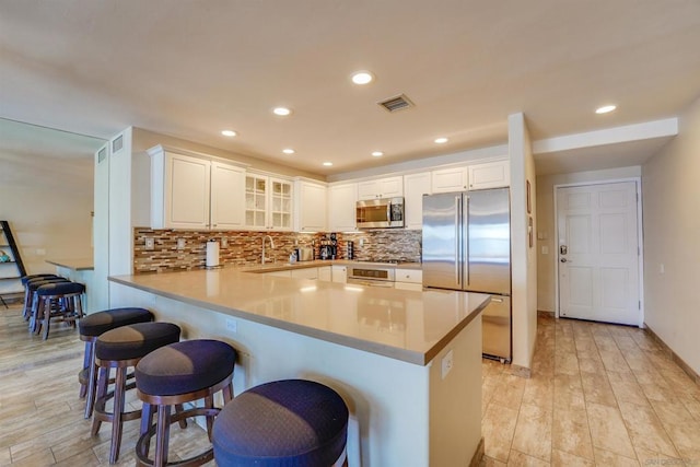 kitchen with a kitchen bar, sink, kitchen peninsula, stainless steel appliances, and white cabinets