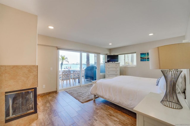 bedroom with a tiled fireplace, access to exterior, and light wood-type flooring