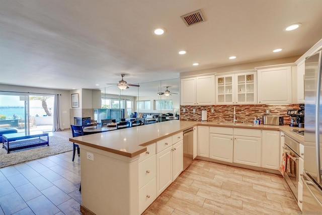 kitchen with sink, white cabinetry, kitchen peninsula, stainless steel appliances, and backsplash