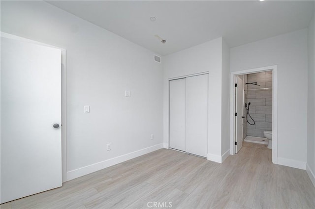 unfurnished bedroom featuring a closet, ensuite bathroom, and light hardwood / wood-style flooring