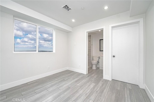 unfurnished bedroom featuring ensuite bathroom and light hardwood / wood-style flooring