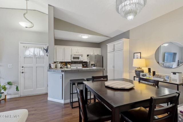 dining area featuring dark wood-type flooring, lofted ceiling, and a notable chandelier