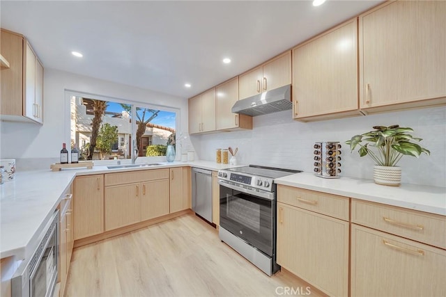 kitchen with sink, stainless steel appliances, tasteful backsplash, light brown cabinetry, and light wood-type flooring