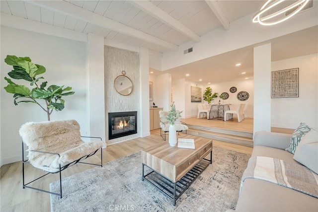 living room with wood ceiling, a fireplace, light hardwood / wood-style floors, and beam ceiling