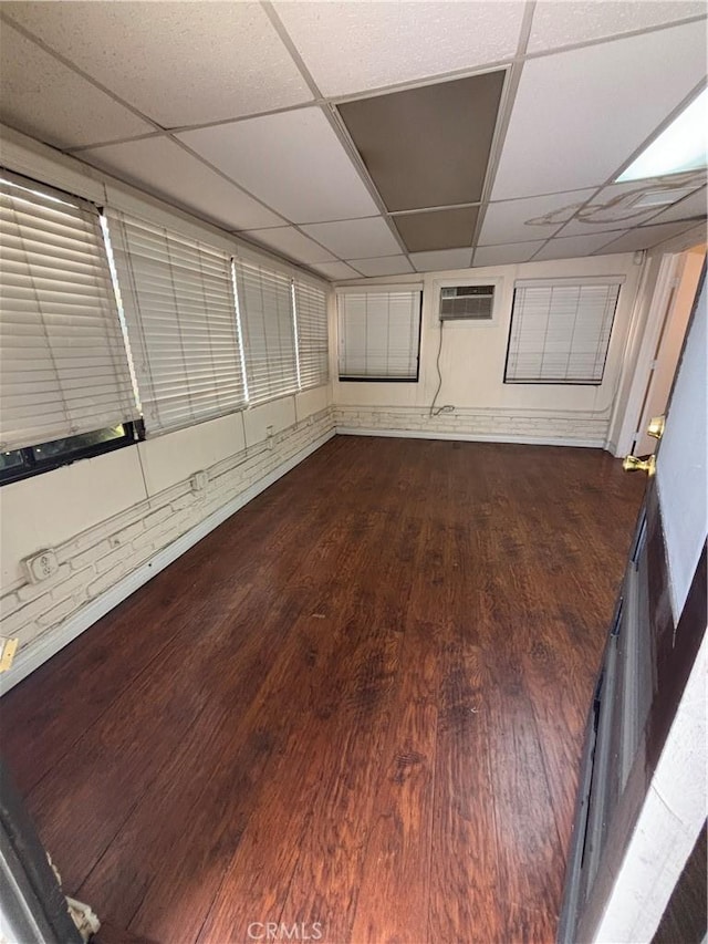 interior space with dark wood-type flooring, a wall unit AC, and a drop ceiling