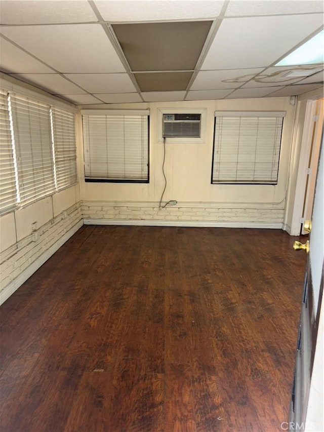 empty room featuring wood-type flooring, a wall mounted AC, and a paneled ceiling