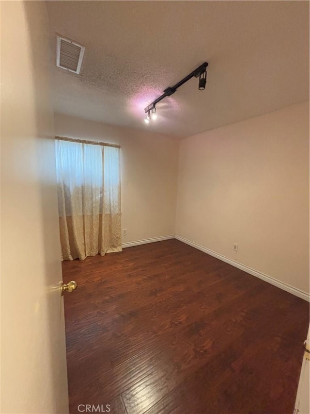 empty room featuring dark wood-type flooring, rail lighting, and a textured ceiling