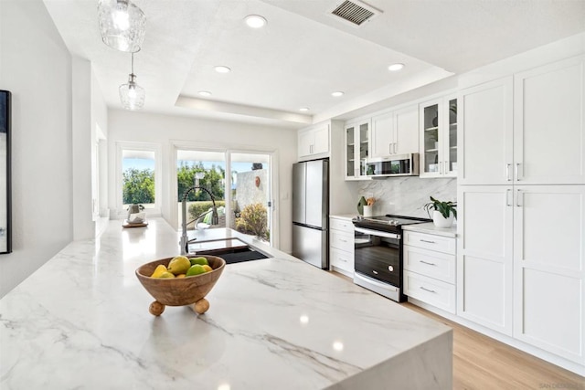 kitchen featuring white cabinetry, hanging light fixtures, a raised ceiling, stainless steel appliances, and light stone countertops