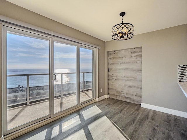 unfurnished dining area with a water view, dark hardwood / wood-style floors, and a notable chandelier