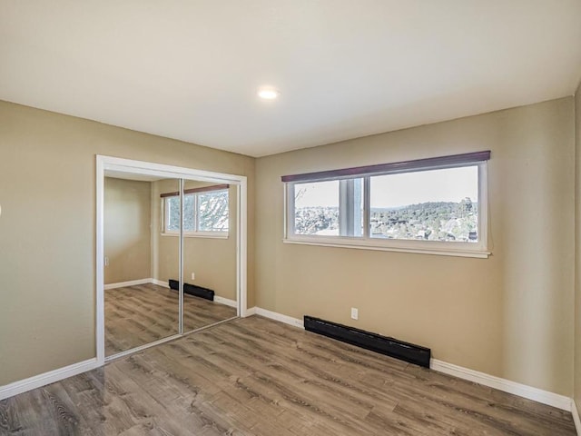 unfurnished bedroom featuring a baseboard heating unit, hardwood / wood-style floors, and a closet