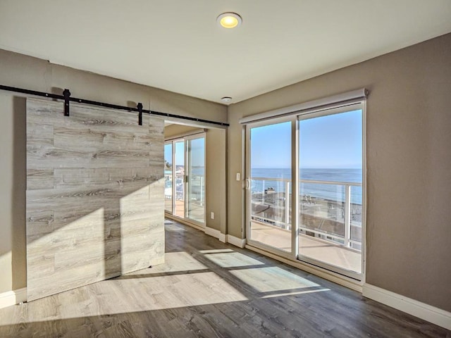 unfurnished room with a water view, wood-type flooring, and a barn door