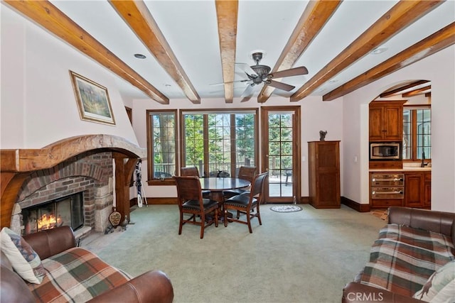 carpeted living room with beamed ceiling, a brick fireplace, and ceiling fan