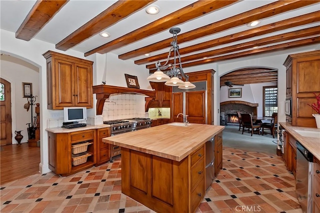 kitchen featuring sink, a kitchen island with sink, stainless steel appliances, wood counters, and decorative light fixtures