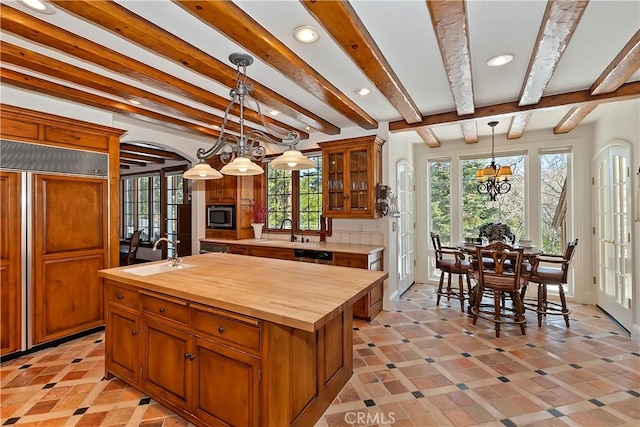 kitchen with sink, wooden counters, built in appliances, a center island with sink, and decorative light fixtures