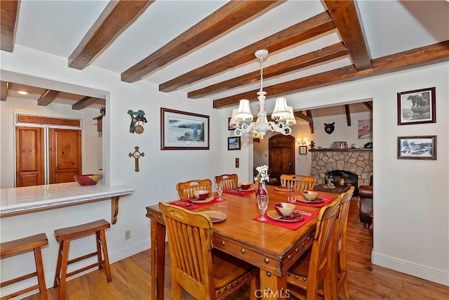 dining area with beam ceiling, a stone fireplace, and light wood-type flooring