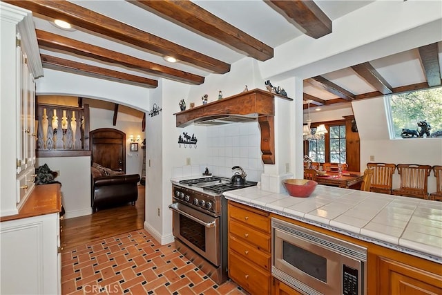 kitchen featuring an inviting chandelier, tile countertops, stainless steel appliances, beam ceiling, and backsplash