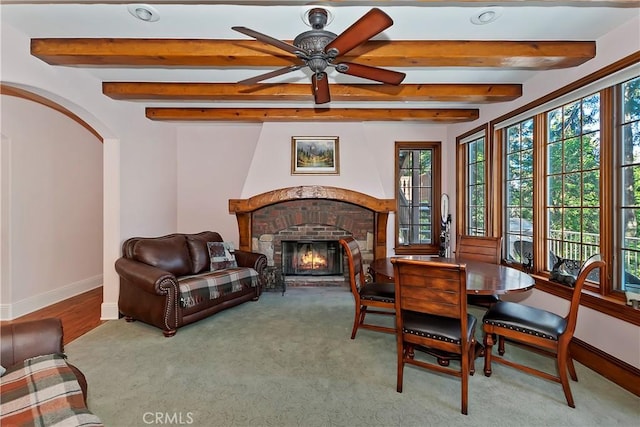 sitting room featuring a brick fireplace, beamed ceiling, and ceiling fan