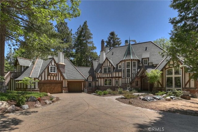 29223 Pigeon Hawk Ln, Lake Arrowhead, CA 92352 - tudor-style house featuring concrete driveway, stone siding, an attached garage, a chimney, and board and batten siding