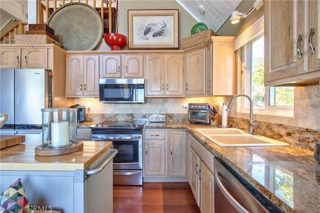 kitchen with appliances with stainless steel finishes, light brown cabinetry, lofted ceiling, sink, and dark wood-type flooring