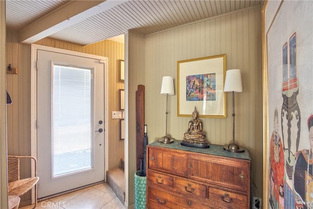 doorway featuring light tile patterned floors, beam ceiling, and wood walls