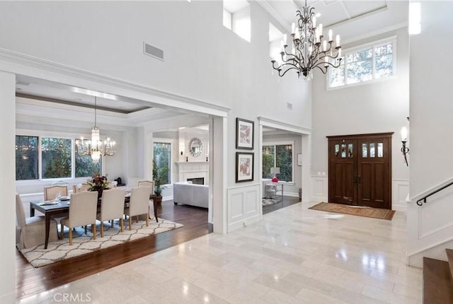 entryway featuring visible vents, a chandelier, a decorative wall, and ornamental molding