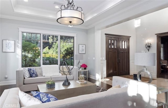 living area featuring ornamental molding, a tray ceiling, baseboards, and wood finished floors