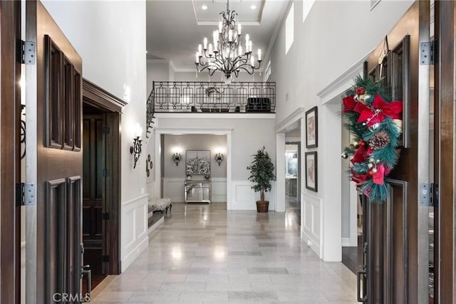 foyer entrance with a chandelier, a decorative wall, a towering ceiling, ornamental molding, and wainscoting