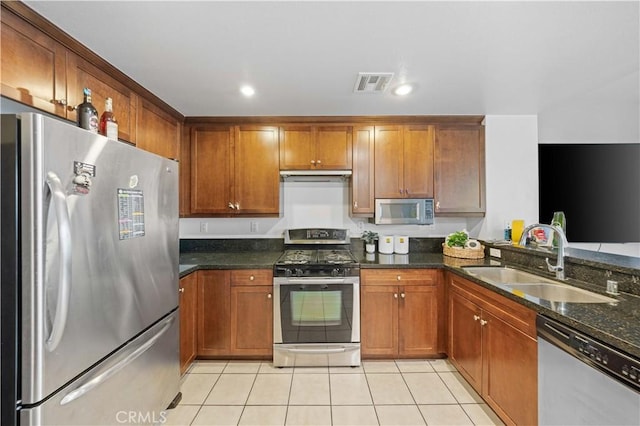 kitchen with sink, light tile patterned floors, dark stone countertops, stainless steel appliances, and exhaust hood