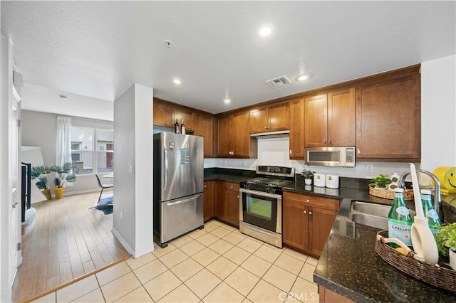 kitchen with appliances with stainless steel finishes, sink, dark stone countertops, and light tile patterned floors