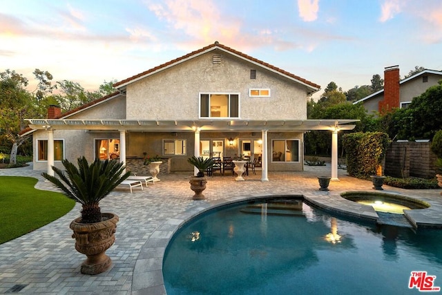 back house at dusk with a pool with hot tub, a patio area, and a pergola